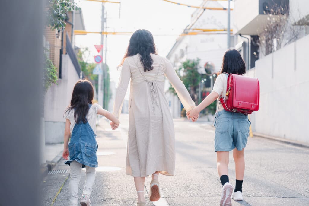 お母さんと手を繋いで学校に行く2人の女の子